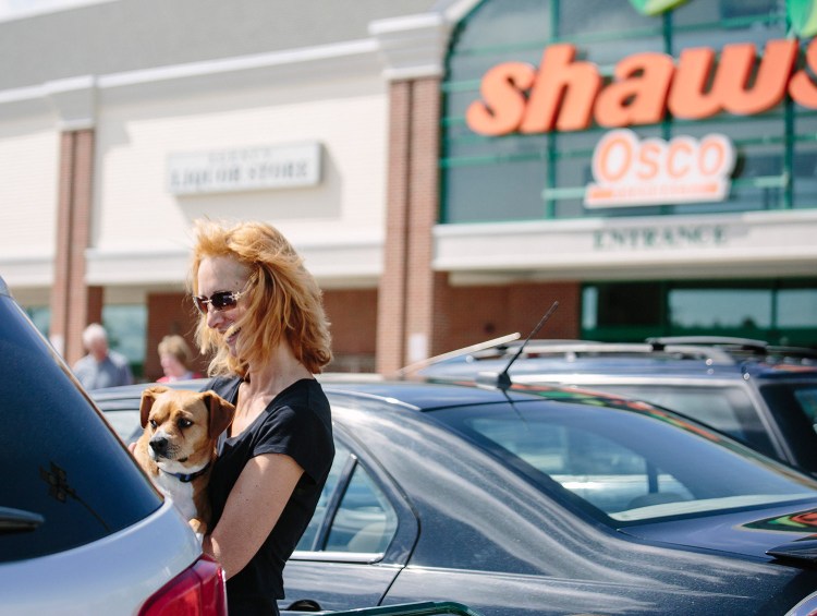 Carey Anne Nason holds her dog Milo after loading groceries from Shaw's into her car in Biddeford on Wednesday. Nason said she shops there because the store's butcher will cut bones small enough for her dog to chew. "I'm disappointed to hear they're closing. I've been coming here since I got Milo three years ago," Nason said.  