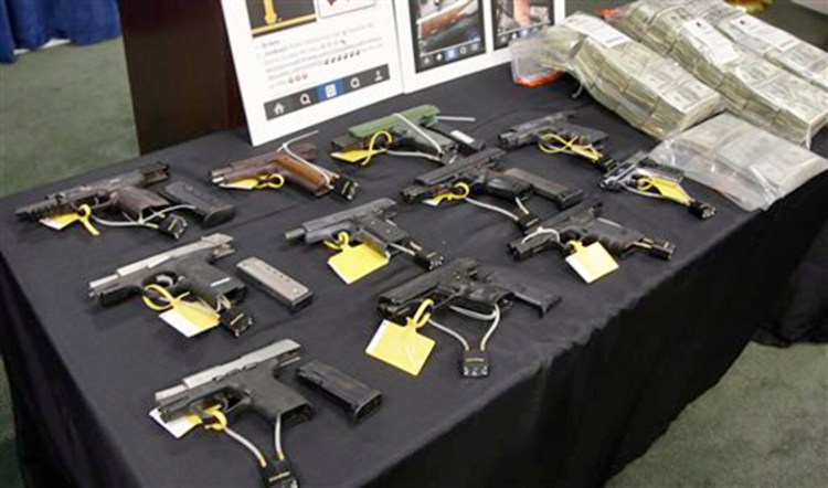 Weapons and money collected during a gang roundup are displayed at a news conference Thursday in Boston. The Associated Press