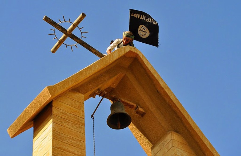 In this photo released March 7 by a militant website, a member of the Islamic State group holds the ISIS flag as he dismantles a cross on the top of a church in Mosul, Iraq.
The Associated Press