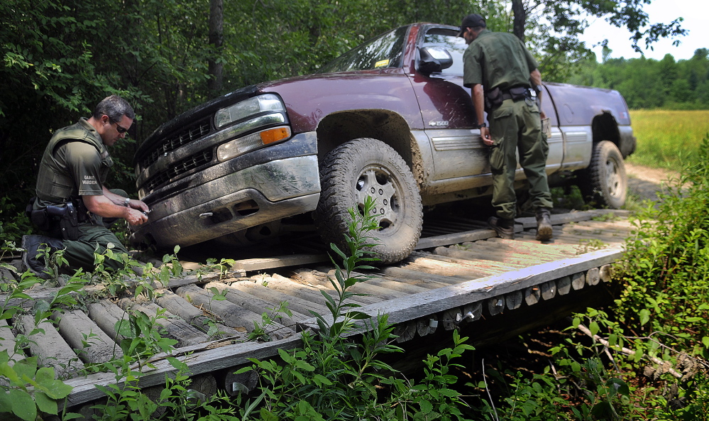 District Game Warden Steve Allarie, left, removes the license plates Sunday as Deputy Game Warden Nick Raymond examines the interior of a pickup that got stuck on an ATV trail in China. The wardens charged the driver for damaging the bridge on private property that is also utilized by snowmobiles, Allarie said.