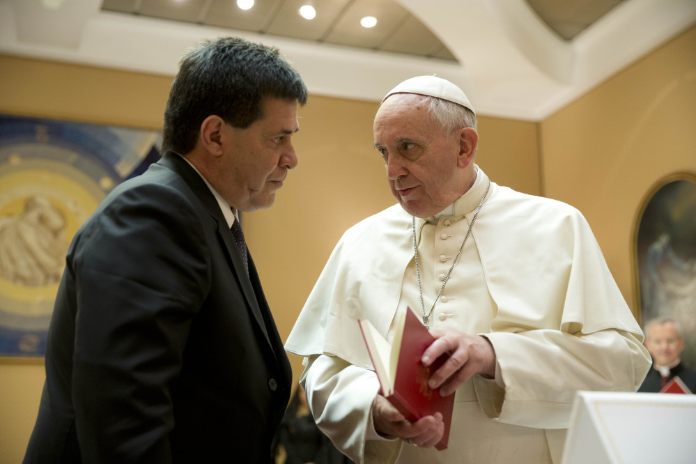 Pope Francis presents Paraguay’s President Horacio Cartes with the book of the gospel during a private audience at the Vatican. The pontiff is making a grueling, weeklong trip that will showcase the pope at his unpredictable best: speaking his native Spanish on his home turf about issues closest to his heart.