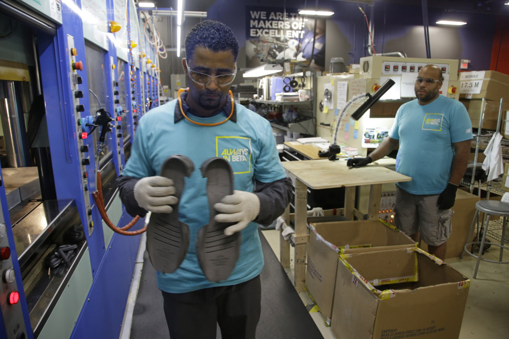 Joao Rodrigues, left, works on pieces of the New Balance 950v2 sneaker, while Loyd Johnson looks on at one of company’s manufacturing facilities in Boston. New Balance wants the Pentagon to honor a 1941 law, known as the Berry Amendment, that requires the Department of Defense to give preference to American-made goods.