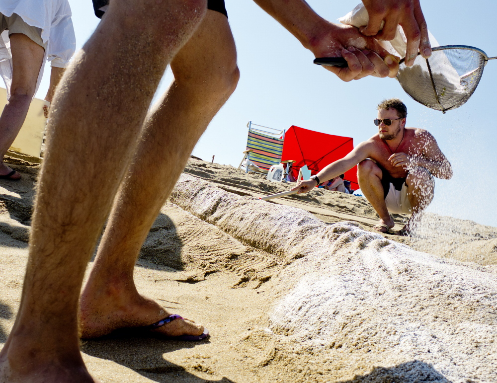Josh Wilson of Montreal, foreground, spreads confectioner’s sugar on a sculpture of the Statue of Liberty as Ben Mortley of Australia works on the crown during the sand sculpture competition Friday.