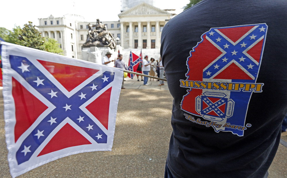 A member of the Sons of Confederate Veterans waves a small Confederate battle flag as he waits for a Save the Flag rally to begin on the steps of the Capitol in Jackson, Miss., on Monday. About 40 people participated in the demonstration.