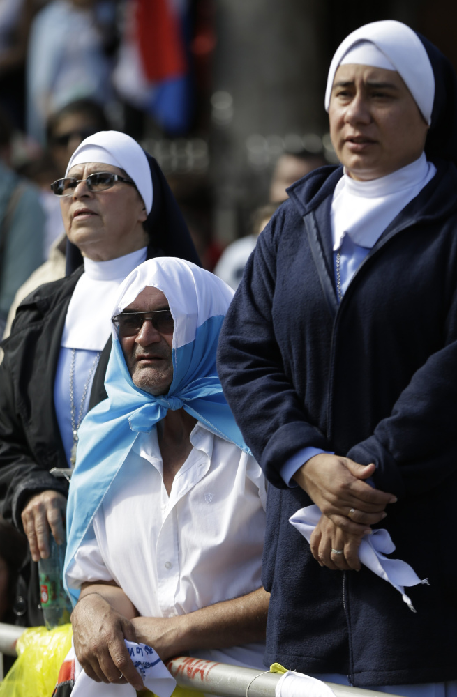 A man shades himself with an Argentine flag between nuns waiting for Pope Francis to arrive to give Mass at the Shrine of the Virgin of Caacupe, in Caacupe, Paraguay, Saturday.
