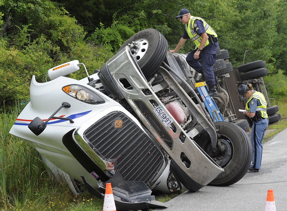 Maine State Trooper Jodell Wilkinson, bottom, takes notes as Cpl. Charles P. Granger of the Commercial Vehicle Enforcement Unit surveys the overturned tractor-trailer. The Department of Public Safety spokesman said the driver likely exceeded the speed limit.