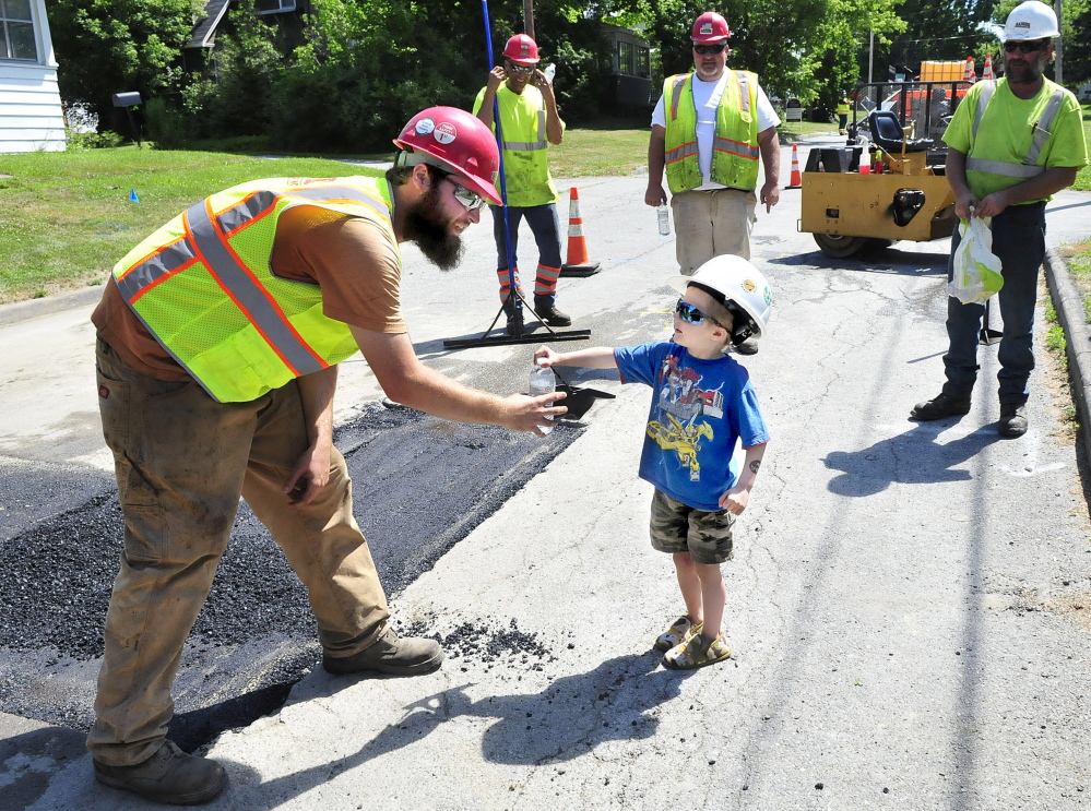 Spencer Murray hands a bottle of water to Ryan Sinclair and other employees working Friday near Murray’s Waterville home. The men have befriended the boy, who regularly showed up to watch them work – and help.