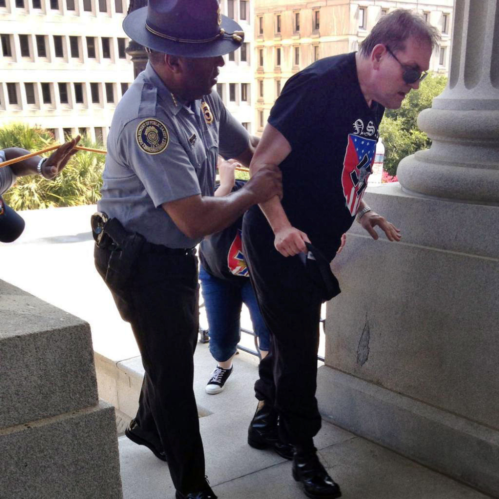 Police officer Leroy Smith, left, helps a man wearing National Socialist Movement attire up the stairs during a rally Saturday in Columbia, S.C.
