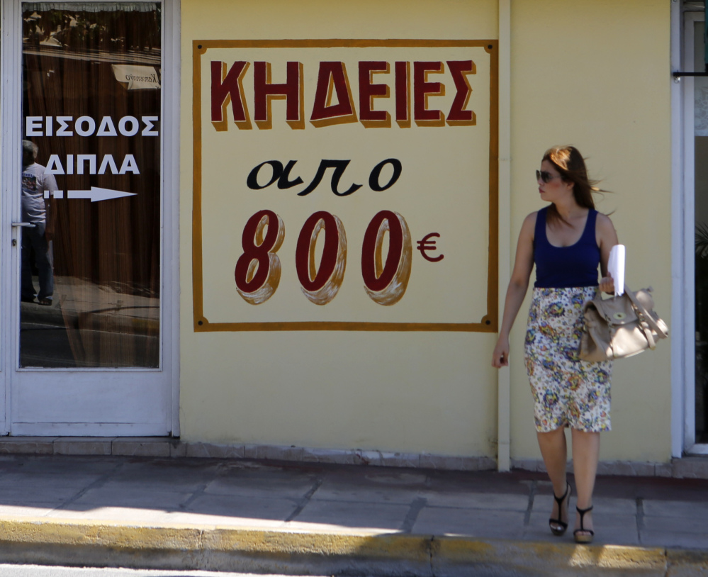A pedestrian waits at a traffic light in Athens as the sign outside a funeral home advertises funerals starting at 800 euros ($866). That’s more than 13 times the daily ATM withdrawal limit under the country’s banking restrictions.