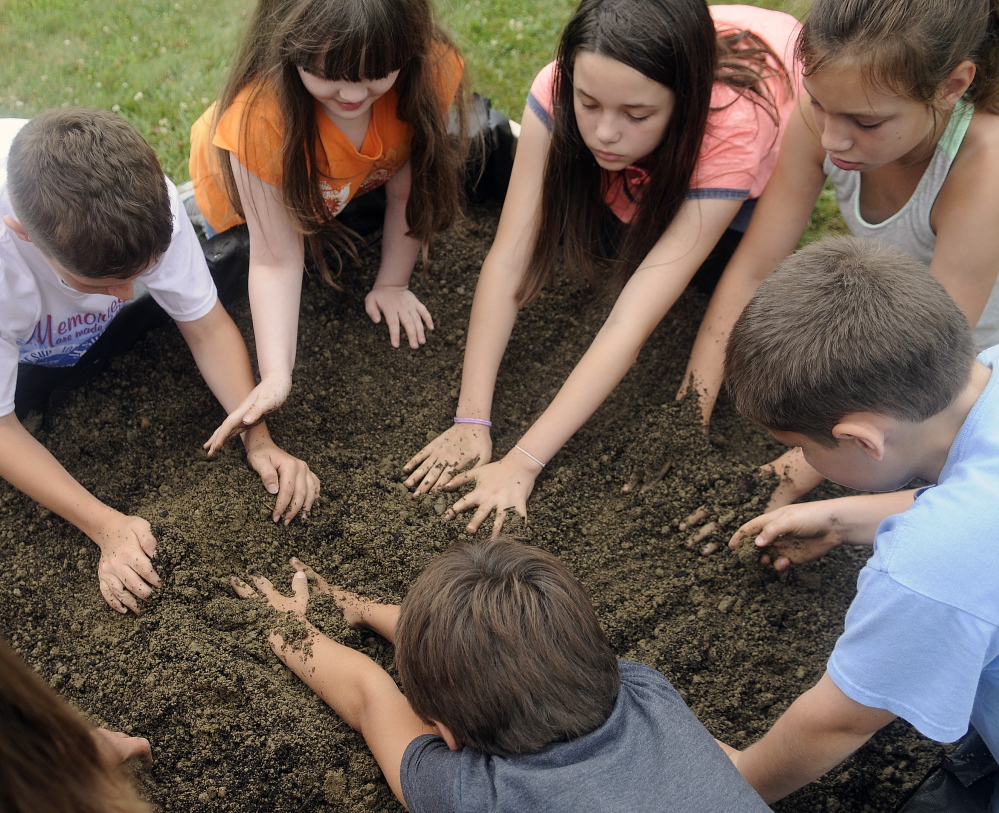 Children mix compost and soil together Monday in the new garden beds at the Buker Community Center in Augusta.
