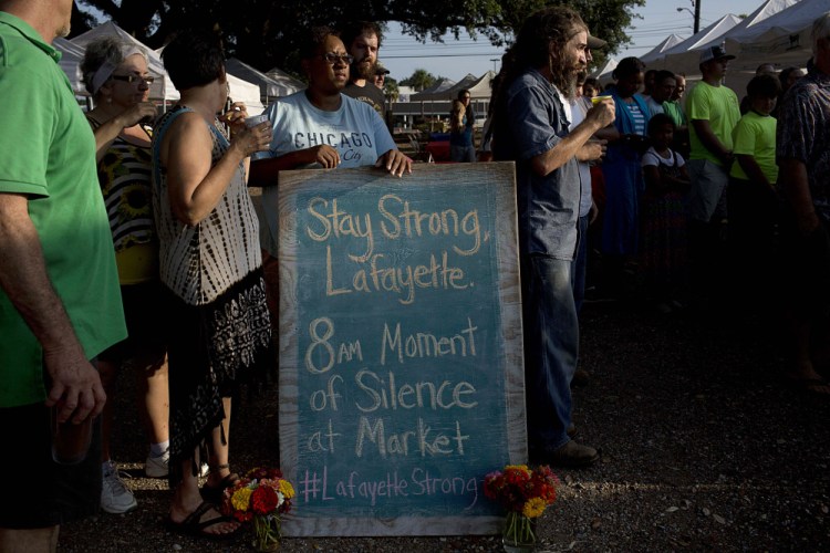 A crowd gathers around a sign for a moment of silence at a local farmers market for the victims of  a deadly shooting at the Grand 16 theatre, Saturday in Lafayette, La.