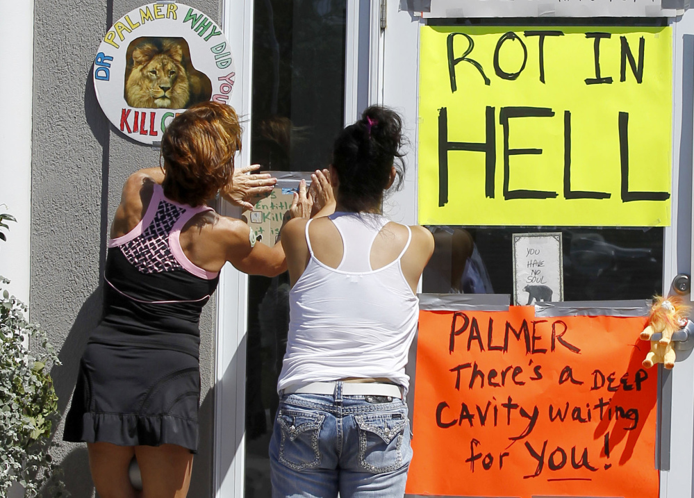 Two women post a sign outside Dr. Walter James Palmer’s dental office in Bloomington, Minn., Wednesday.