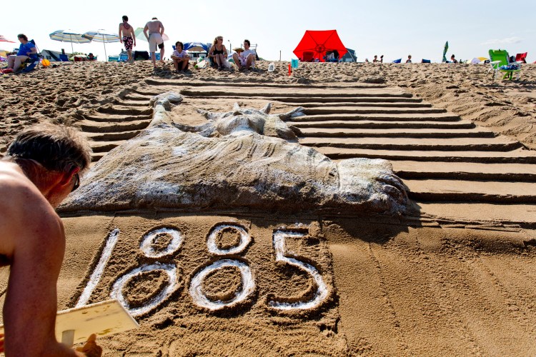 Peter Wilson, 58, of Montreal writes “1885” at the base of his team’s sand sculpture of the Statue of Liberty during the 29th annual Family Sand Sculpture Competition in Ocean Park on Friday. Wilson’s family has been vacationing in Ocean Park for 86 years and has taken part in the sculpture competition for many years.  Gabe Souza/Staff Photographer