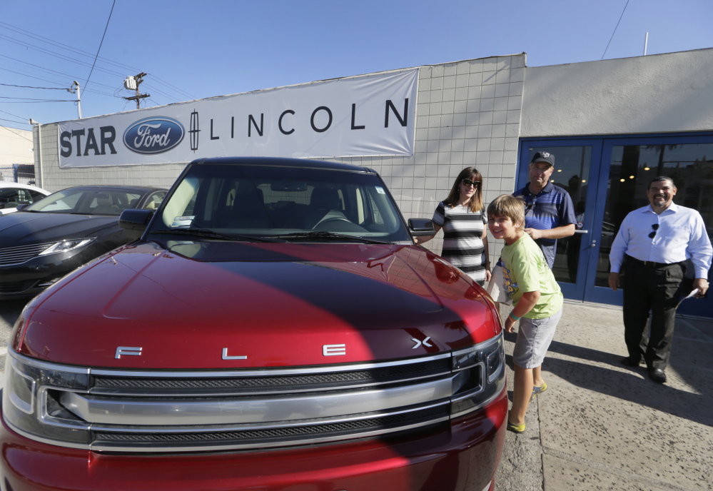 Robert Schemer, his wife, Kelly, and their son Graham, 9, pose next to their newly purchased pre-owned 2013 Ford Flex Limited, at the Star Ford Lincoln dealership in Glendale, Calif. At right is sales consultant Allan Calix. Summer deals and big demand for SUVs and luxury vehicles kept U.S. auto sales strong in July, according to reports released, Monday.