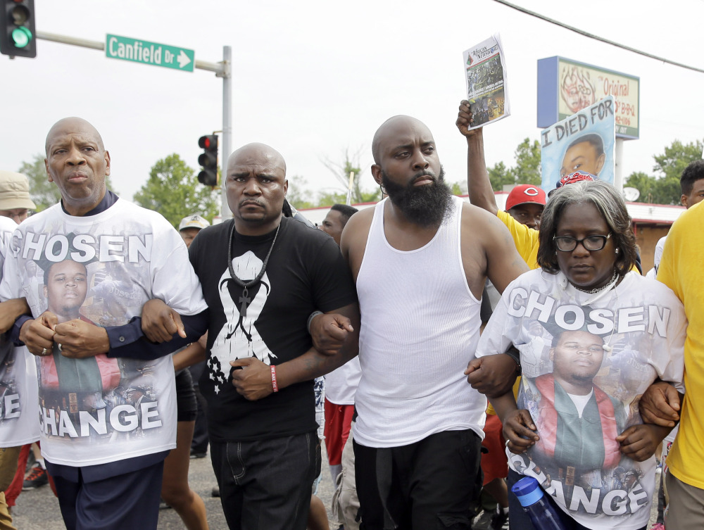 Michael Brown Sr., in a white tank top, locks arms with others as he takes part in a parade in memory of his son, Michael Brown, Saturday, in Ferguson, Mo., where several events are marking the one-year anniversary of the fatal shooting.