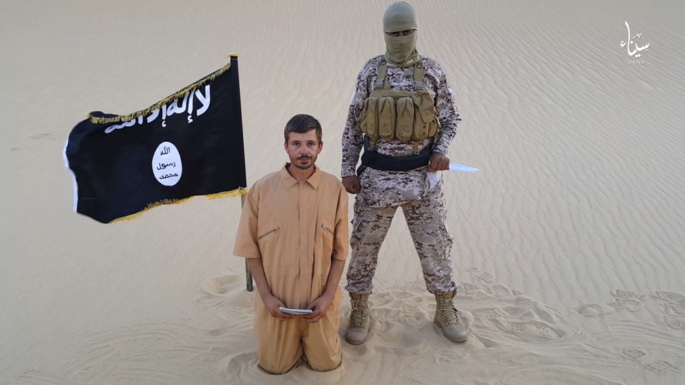 This image made from a militant video posted on a social media site on Wednesday, Aug. 5, 2015, which has been verified and is consistent with other AP reporting, purports to show a militant standing next to another man who identifies himself as 30-year-old Tomislav Salopek, kneeling down as he reads a message at an unknown location.