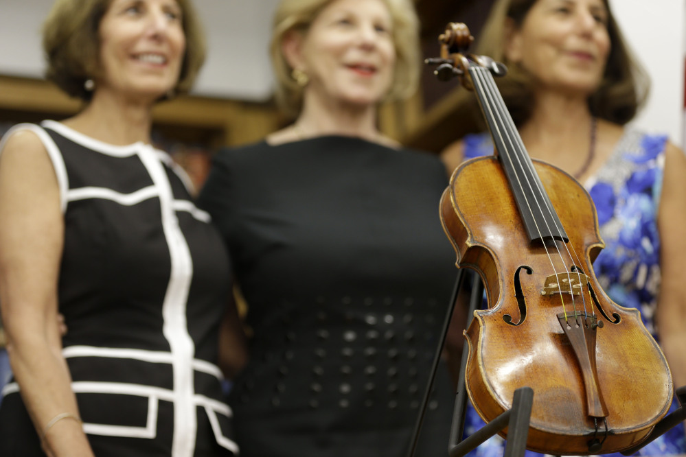 Sisters Jill Totenberg, left, Nina Totenberg, center, and Amy Totenberg pose for pictures with the recovered Ames Stradivarius violin during a news conference in New York, Aug. 6.