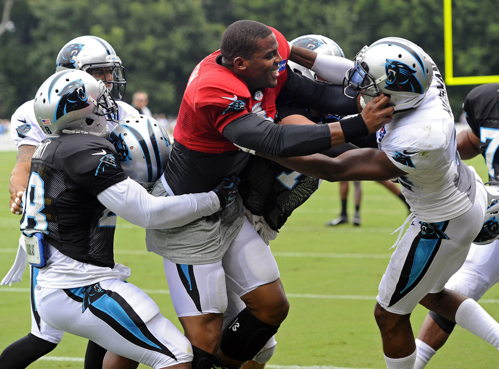 Cam Newton, center, wears the red jersey quarterbacks wear in practices, meaning they can’t be touched. But that didn’t stop him from going after cornerback Josh Norman, right, after taking a stiff-arm in a Carolina practice. And Newton said he’d do it again.