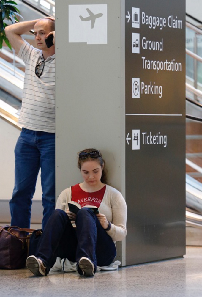 Carrie Kolar, right, reads as her boyfriend Matthew DiPrima, left, tries to make alternate travel plans to get home to Washington, D.C.,  from the Portland International Jetport on Saturday.