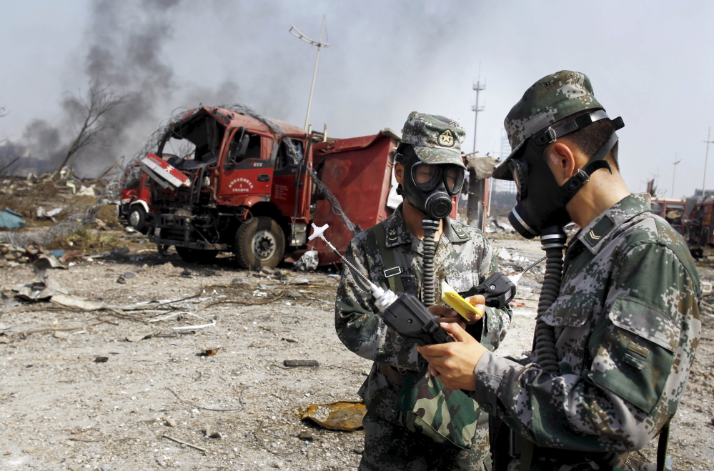 Soldiers of the People’s Liberation Army anti-chemical warfare corps work next to a damaged firefighting vehicle at the site of Wednesday night’s explosions in Tianjin, China.