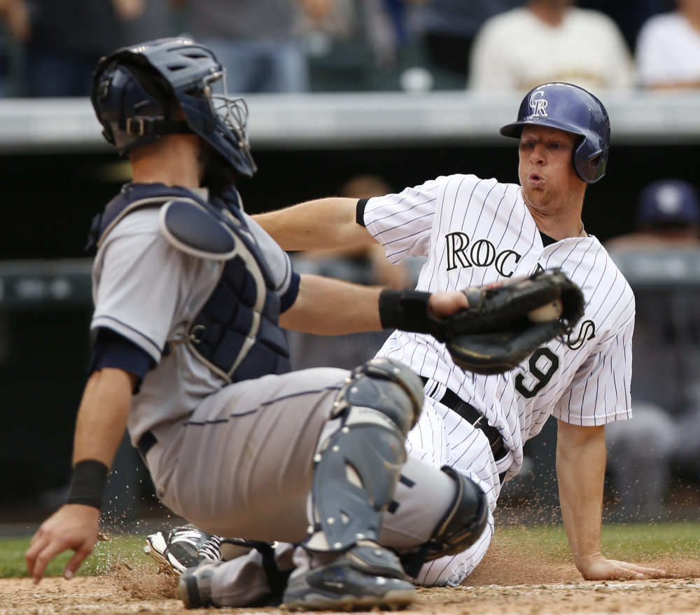 Colorado’s DJ LeMahieu slides past the tag of San Diego catcher Austin Hedges in the seventh inning of the Rockies’ 5-0 win Sunday in Denver.