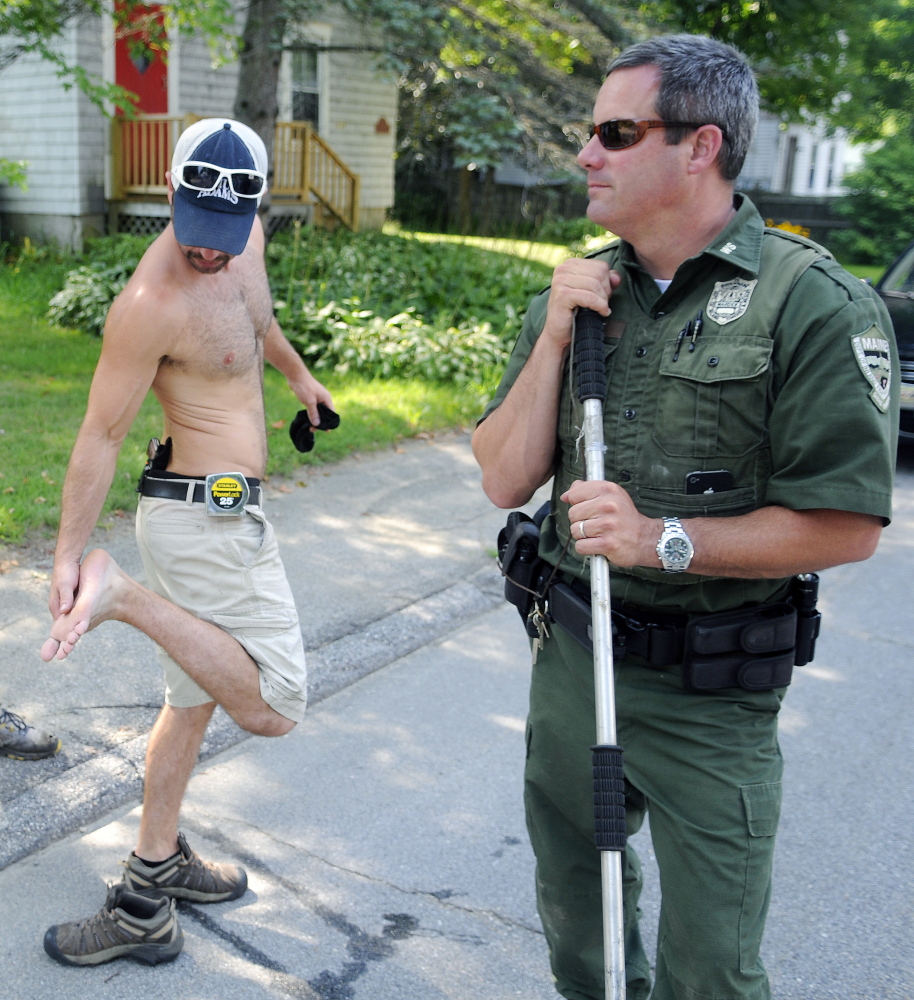 Jared Stevens inspects his foot Monday after a gray fox bit his sneaker on the steps of his Monmouth home. District Game Warden Steve Allarie searched for the animal that also bit another person. Stevens put a pistol in his waist band after the attack.