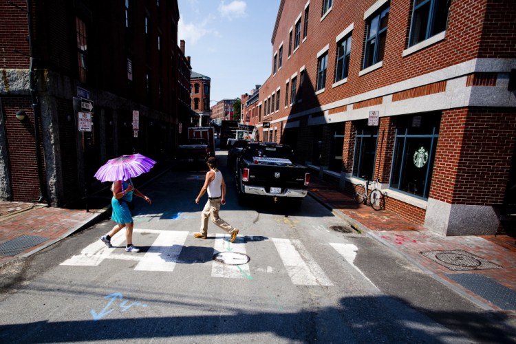 A woman uses an umbrella to keep the sun off as she tries to beat the heat on Commercial Street in Portland on Monday.