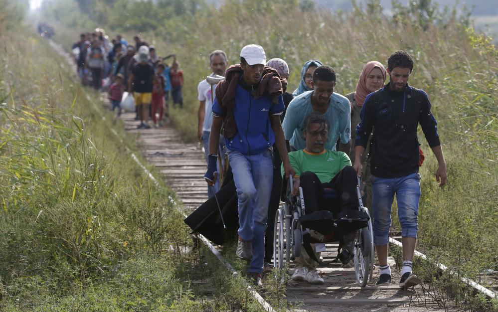 Migrants assist a wheelchair user as they traverse a railway track near the Serbian border with Hungary, near Horgos, Serbia, on Tuesday. A new wave of people fleeing war-torn countries in the Middle East and Africa is straining resources in some European countries.