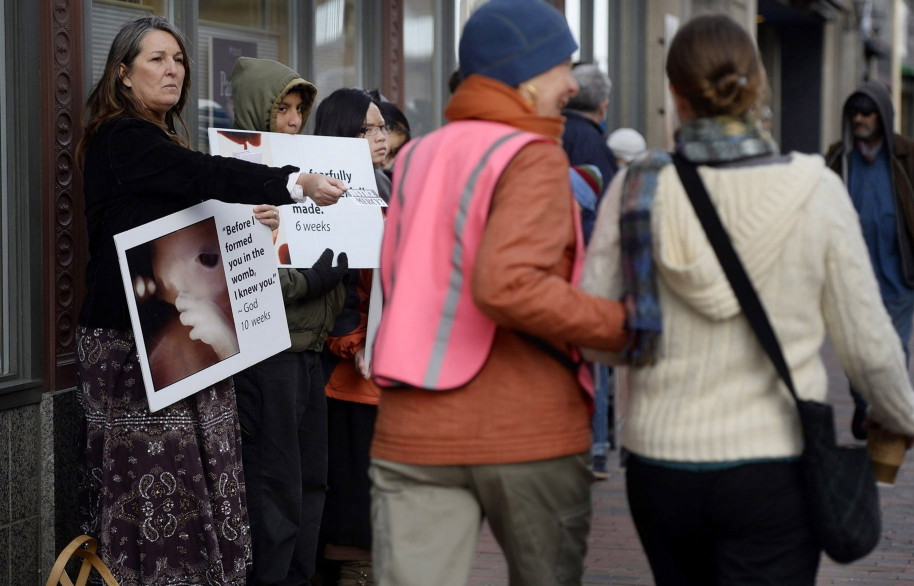 Joan McDonald, wearing a pink vest, escorts a pedestrian past abortion protesters, including Leslie Sneddon, left, of Richmond, outside the Planned Parenthood clinic on Congress Street in Portland.