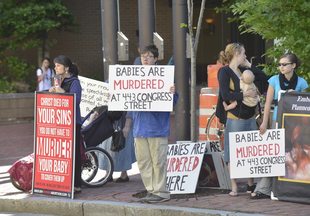Anti-abortion protesters hold up signs across the street from the Planned Parenthood clinic on Congress Street in Portland.