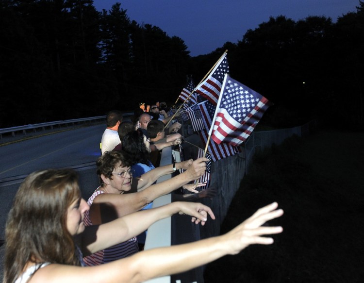 Well-wishers wave American flags while they wait on a Maine Turnpike overpass in Arundel on Saturday for a procession escorting the remains of Corey Dodge back to Maine. The Garland man was killed in Afghanistan last weekend. Story, B3