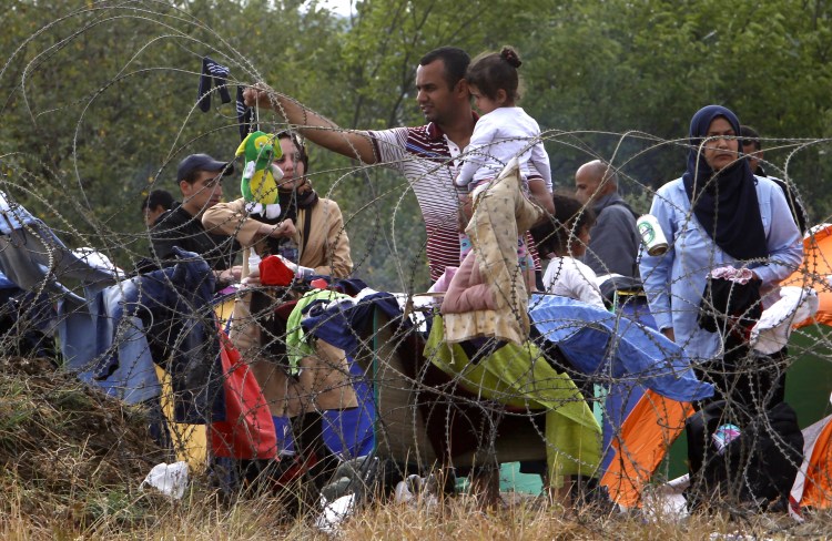 A migrant holding a child hangs a stuffed toy on barbed wire to dry after the rain while waiting to enter Macedonia from Greece on Saturday. The Associated Press
