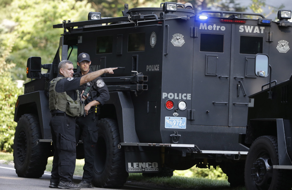Law enforcement officials talk beside an armored vehicle Wednesday after multiple shots were fired into a Millis police cruiser in Millis, Mass. Police say the cruiser then crashed into a tree and caught on fire. No injuries were reported. The investigation is continuing.