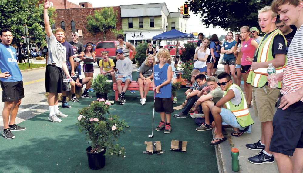 Surrounded by Colby College students, Zachary Wentworth of Clinton, center, eyes his golf shot at the “relaxation” park set up in downtown Waterville as an orientation project by incoming students on Thursday. Student Andrew Destaebler raises his arm as the ball goes in.