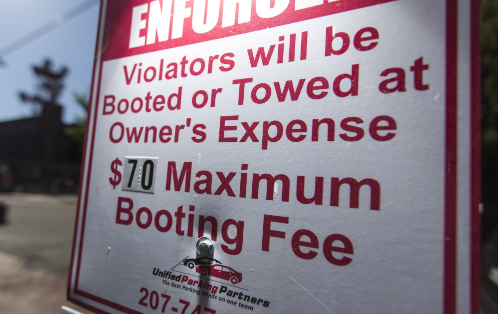 A sign at a Unified Parking Partners lot on Shepley Street warns of the consequences of violations. The company has been under fire for its booting practices, but now says it will relax its practice of booting vehicles with expired parking tickets.