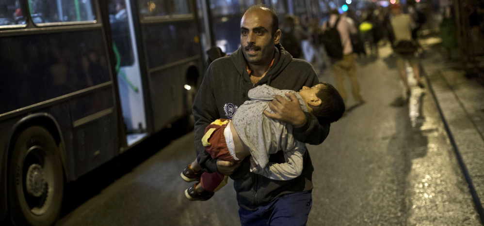 A man carries a child as he runs to board a bus provided for refugees in Hungary after Austria said that it and Germany would let them in.