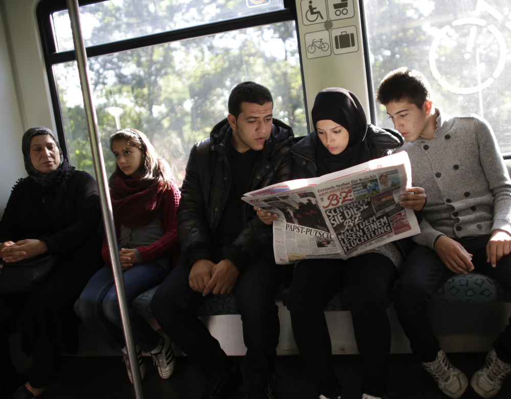 Syrians Reem Habashieh, flanked by her brothers Yaman, right, and Mohammed, ride a train in Berlin while reading a newspaper with special pages in Arabic for refugees. At left is the siblings’ mother, Khawla Kareem, with 11-year-old daughter Raghad.