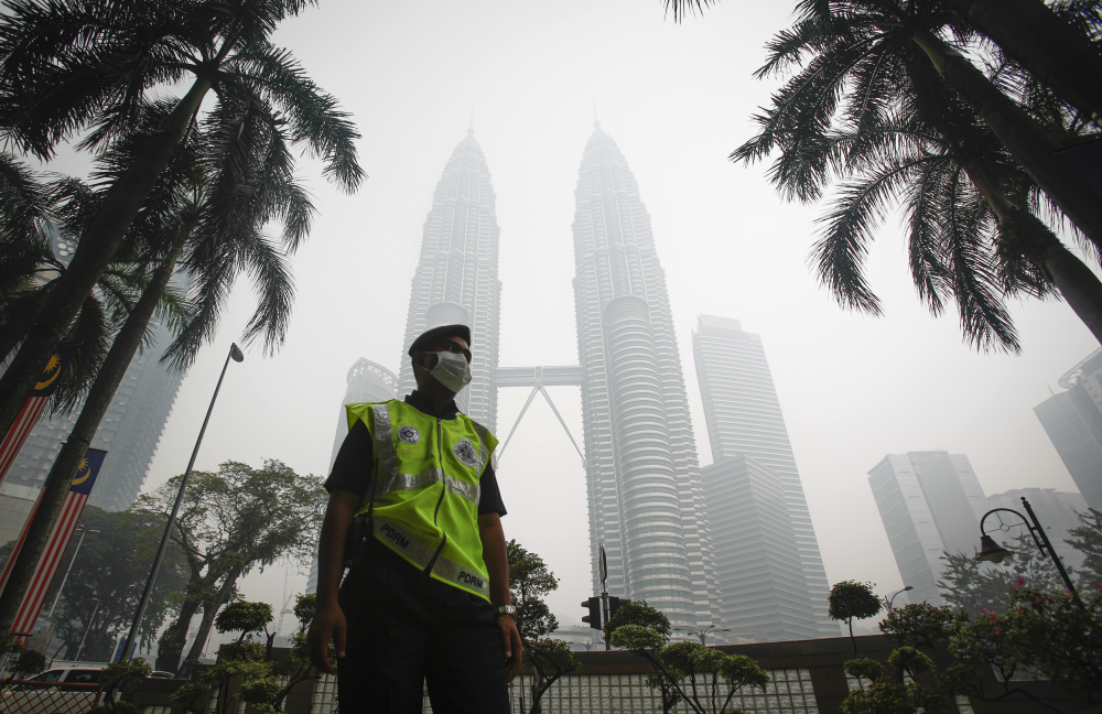 A masked Malaysian police officer stands guard in front of Petronas Twin Towers shrouded by haze in Kuala Lumpur, Malaysia. on Monday.