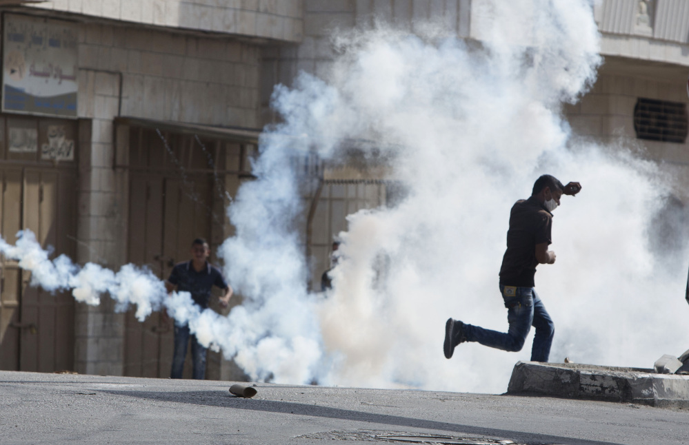 A Palestinian man runs for cover from tear gas fired by Israeli soldiers after a demonstration Tuesday in solidarity with Jerusalem protesters in the West Bank town of al-Ram.