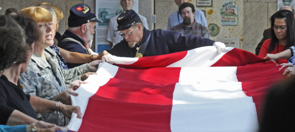 Historians and others fold an 18-by-33-foot replica of an 1860 Fort Sumter garrison flag during a ceremony on Wednesday in the Maine State Cultural Building in the State House complex in Augusta.