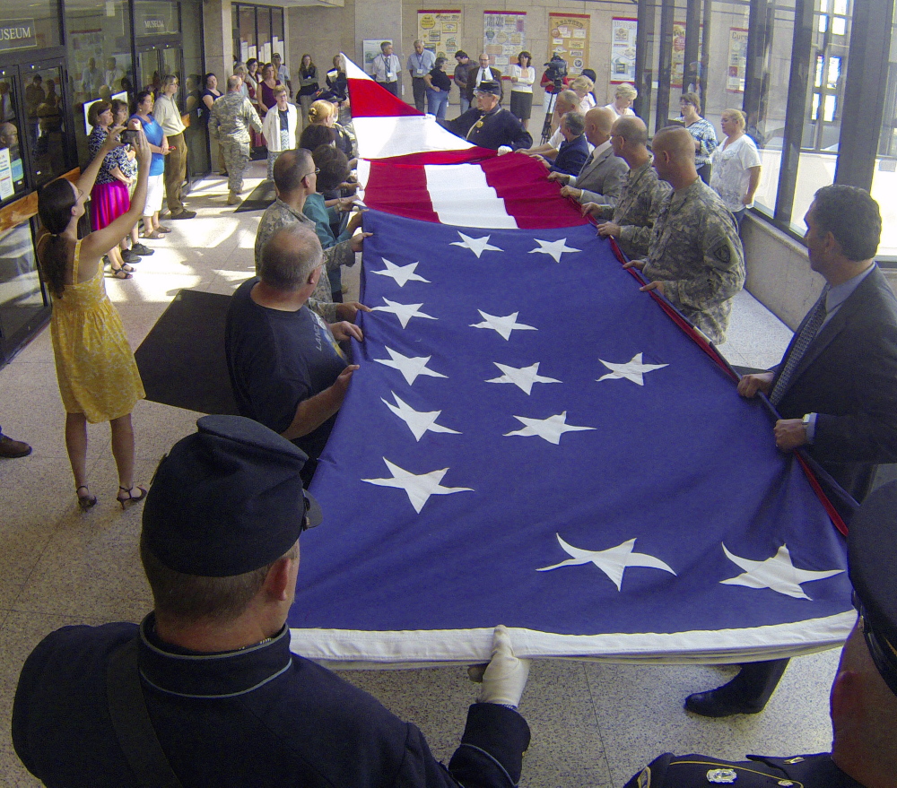 Civil War re-enactors and others fold an 18- by 33-foot replica of an 1860 Fort Sumter garrison flag during its retirement ceremony Wednesday in the Maine State Cultural Building in Augusta.