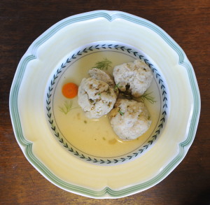 Ali Waks-Adams makes matzoh balls that contain an unusual ingredient: horseradish leaves. Three sit in a bowl with broth. The small green specks are the horseradish leaves.