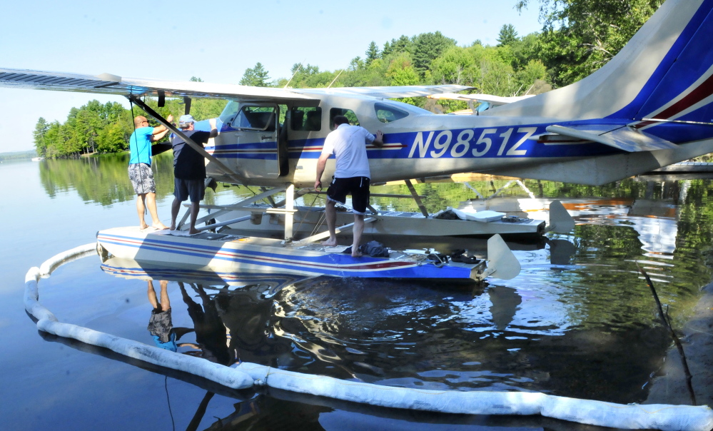 Pilot Don Stoppe, left, helped by passenger Perry Bryant, opens the engine compartment to his plane, which was forced to land Thursday on Wesserunsett Lake in East Madison after the engine’s oil pressure dropped. Stoppe’s brother and passenger Rick Stoppe is at right. Oil containment pads in the water surround the plane.