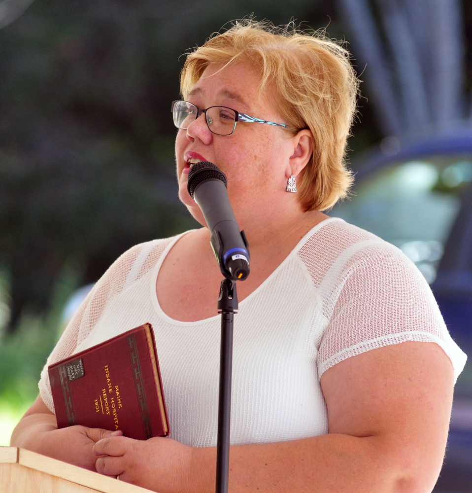 Simonne Maline, executive director of the Consumer Council System of Maine, holds a copy of a 1901 Maine Insane Hospital report as she speaks during a dedication of a marker Friday in memory of people who died at the former Augusta Mental Health Institute at Cony Cemetery in Augusta.