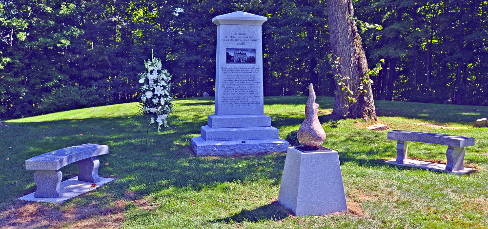A stone sculpture of an eternal flame stands in front of the monument in honor of people who died at the former Augusta Mental Health Institute before a dedication Friday at Cony Cemetery in Augusta.
