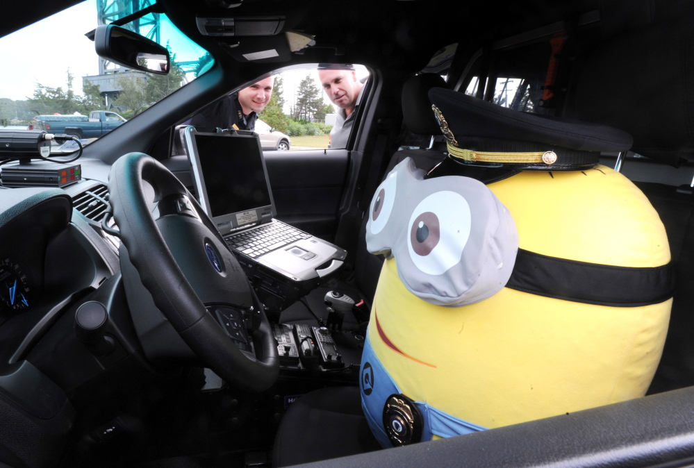 Bourne Lt. Brandon Esip, left, and Detective Sgt. John Stowe look at the Minion doll they use on Facebook to pass along department information. It’s this kind of goofy, imaginative content that has made the police department’s Facebook page popular.
