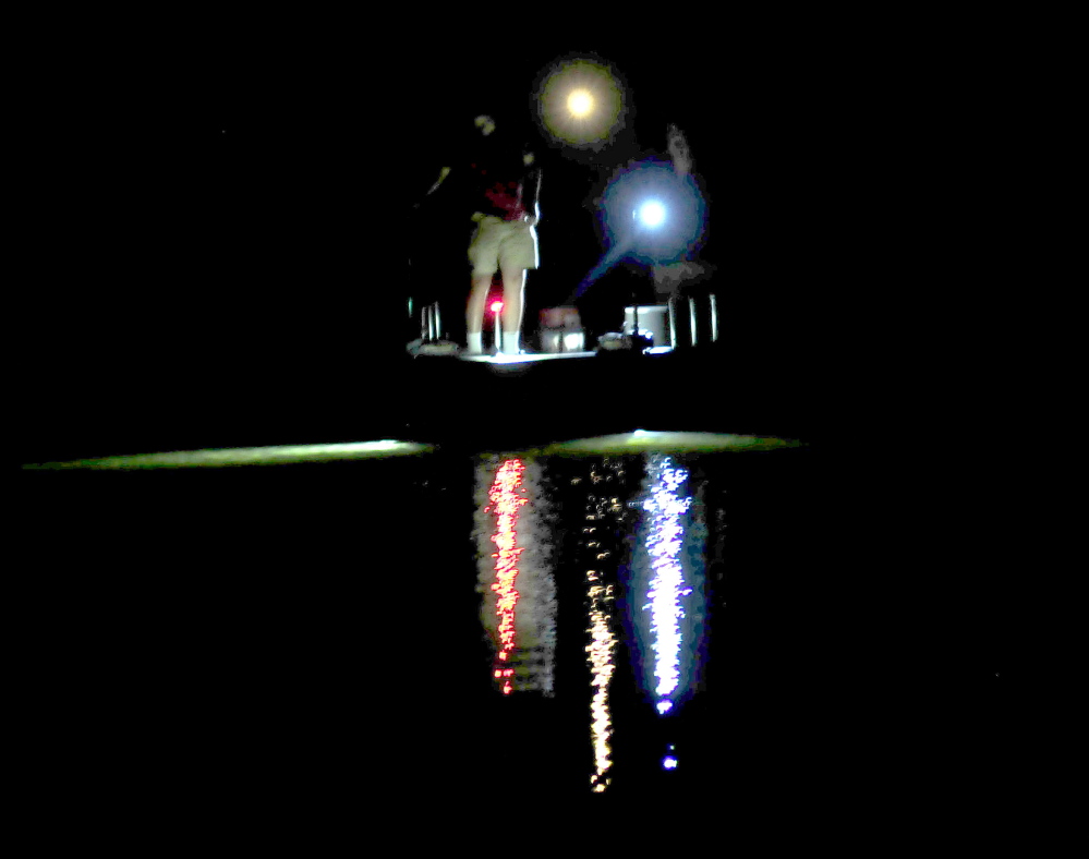 A Belgrade Regional Conservation Alliance boat and group members are illuminated by lights both on board the boat and in the water while searching for milfoil plants Thursday evening in Great Pond in Belgrade.