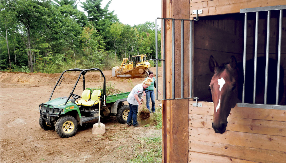 Stephanie Wrigley, left, and Milynn Phair, members of Halee Cummings’ family, pick up loose material Tuesday as a bucket loader operator creates a family cemetery at the Paquette farm in Sidney. Cummings died Friday in an all-terrain vehicle accident nearby. One of her horses looks out of his stall.