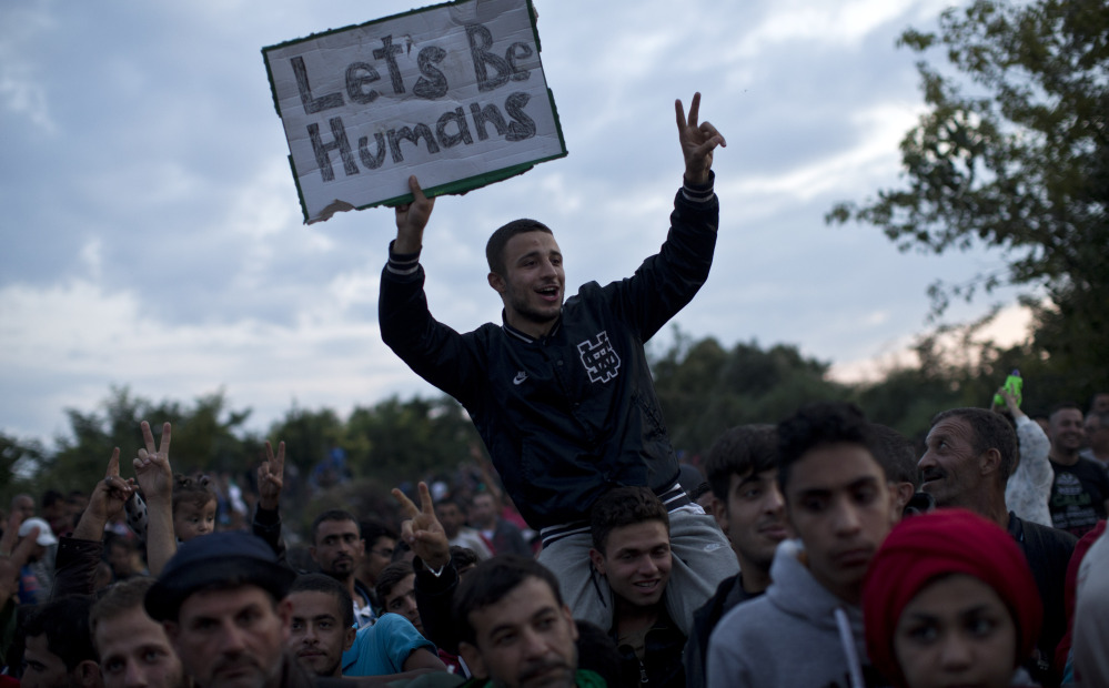 A man holds a sign reading “Let’s be Humans” as he waits along with other migrants to be boarded onto buses in the town of Babska, Croatia.