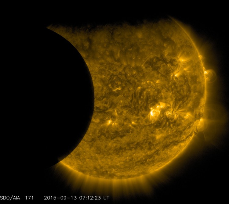 The moon, left, and the Earth, whose edge is visible at top, transit the sun (colorized in gold) together on Sept. 13, as seen from the Solar Dynamics Observatory. The edge of Earth appears fuzzy because the atmosphere blocks different amounts of light at different altitudes. This is an image of the three bodies taken from a space-based observatory.